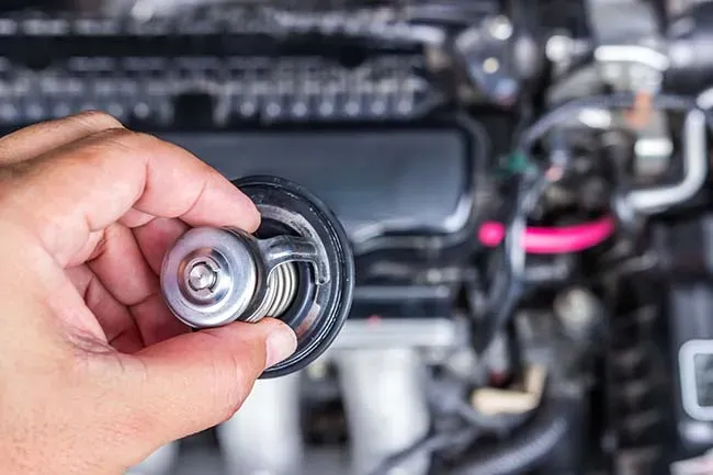 Mano sosteniendo termostato de temperatura de motor