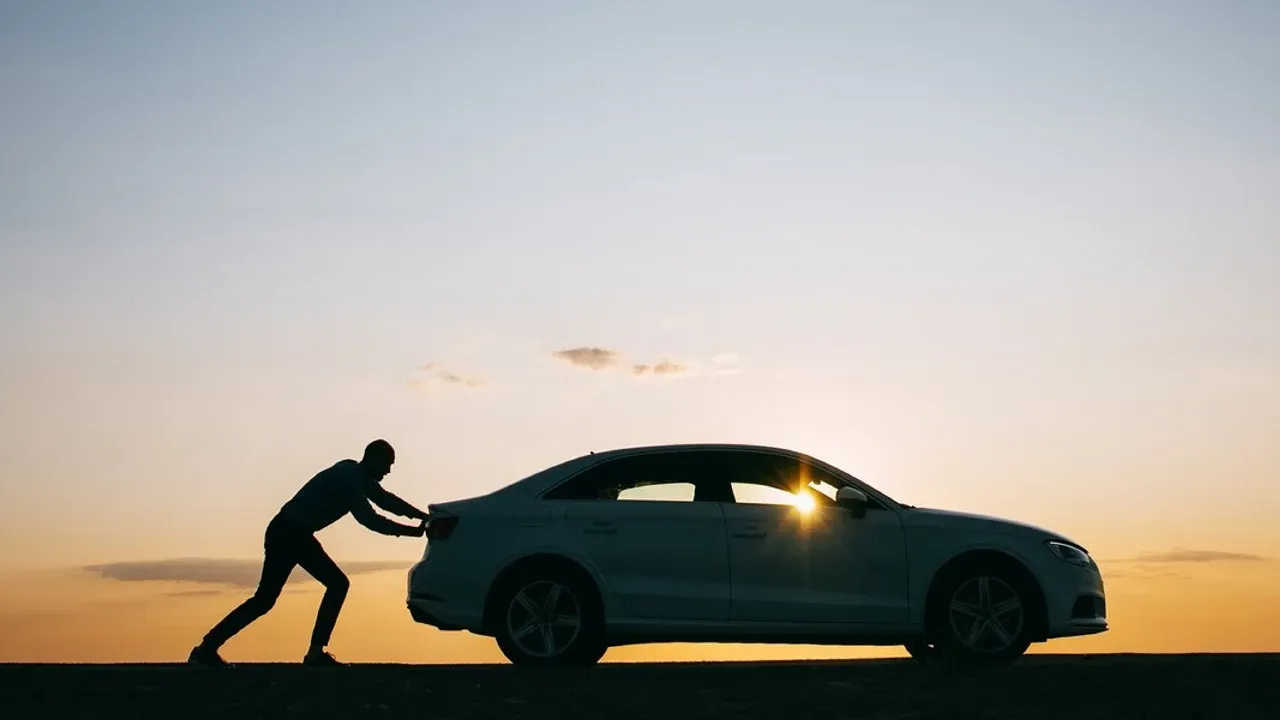 Persona empujando auto en una puesta de sol