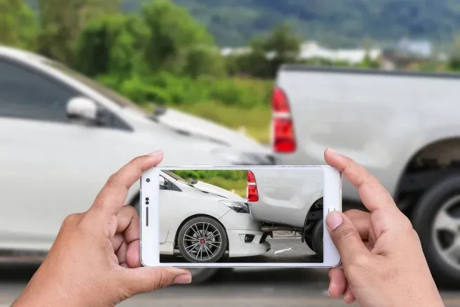 Manos sosteniendo teléfono que toma una foto a choque entre auto y camioneta