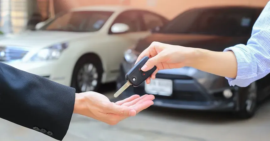 Persona entregando llave de auto a otra y al fondo dos autos