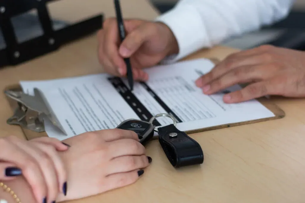 Dos personas llenando documento en mesa con llaves de auto