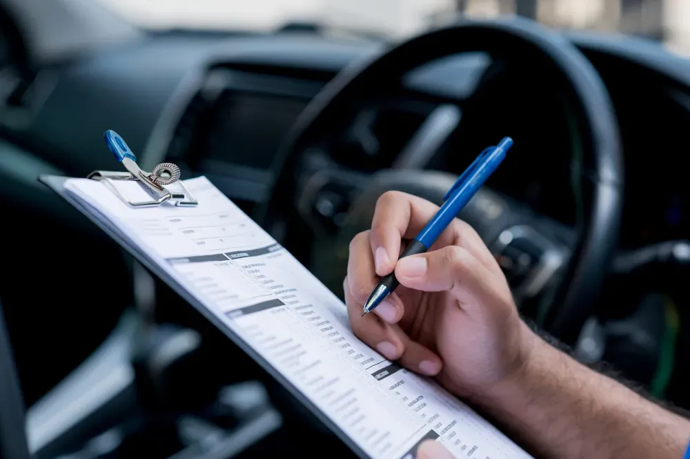 Mano sosteniendo tabla con papel y bolígrafo al fondo interior de un auto