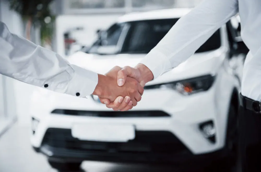 Personas estrechando sus manos y al fondo una camioneta blanca