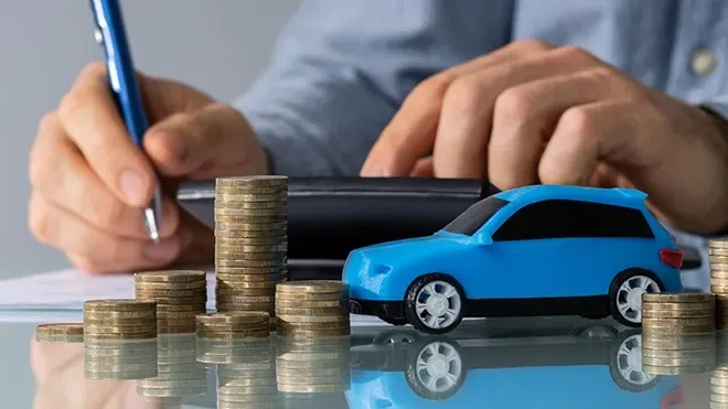 Auto azul junto a monedas y unas manos sosteniendo un bolígrafo sobre papel