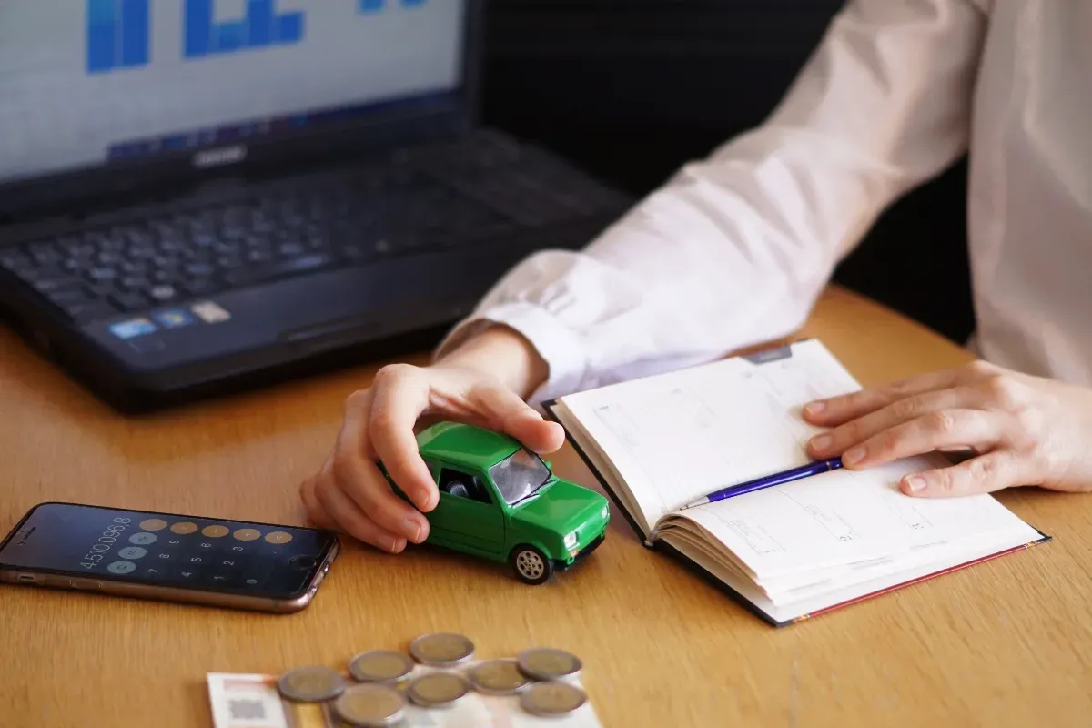 Persona tomando auto verde de escala y un libro con bolígrafo en una mesa