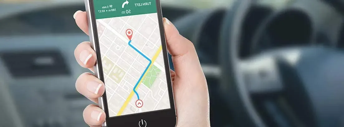 Mano sosteniendo teléfono con GPS activado y de fondo el interior de un auto