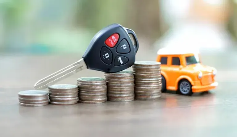 Llave de auto sobre pilas de monedas y al lado un auto naranja 