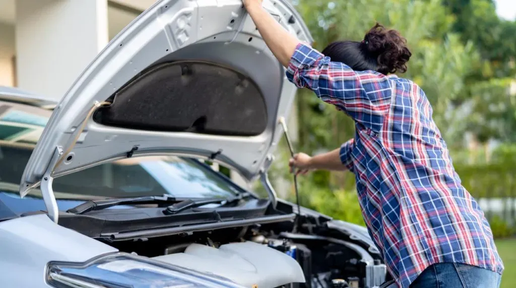 Persona levantando capo de auto y revisándolo 