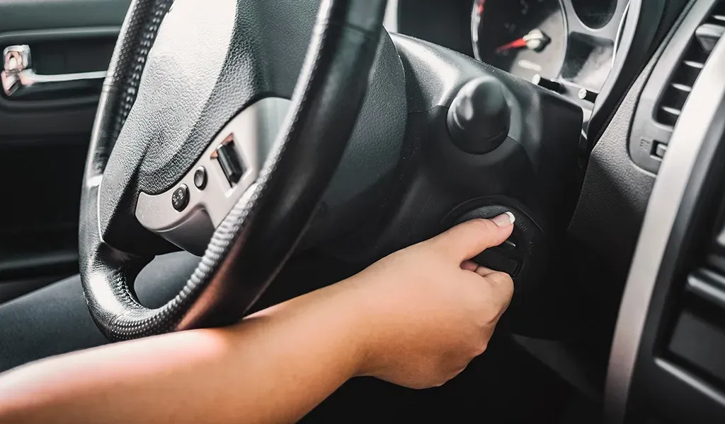 Mano girando llave en auto para encenderlo 