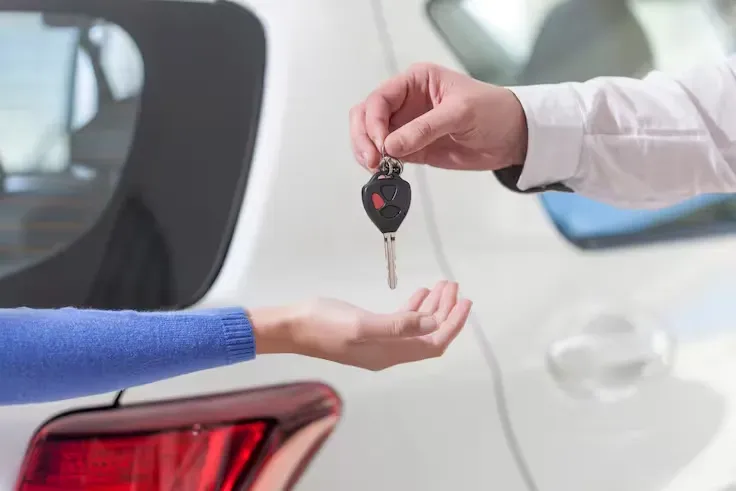 Entrega de llave de autos a una persona y de fondo un auto blanco