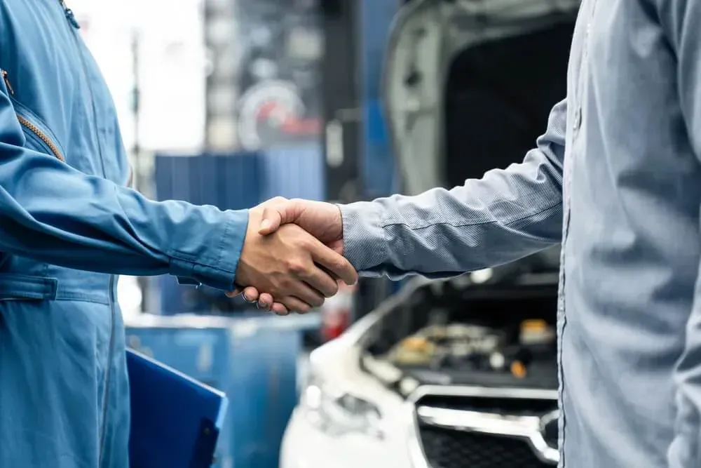 Personas estrechando la mano y al fondo auto con capo levantado 