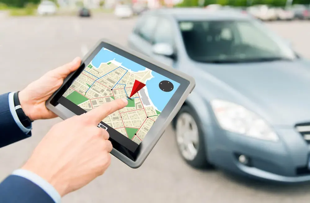 Mano sosteniendo Tablet que proyecta localización GPS y de fondo un auto 