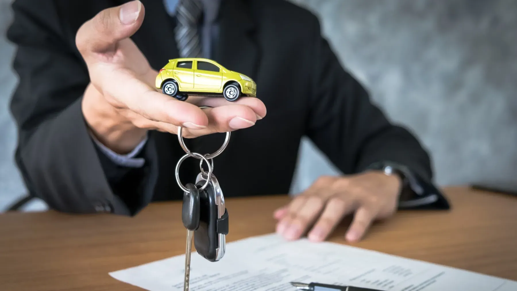 Persona entregando llaves de auto y auto amarillo a escala