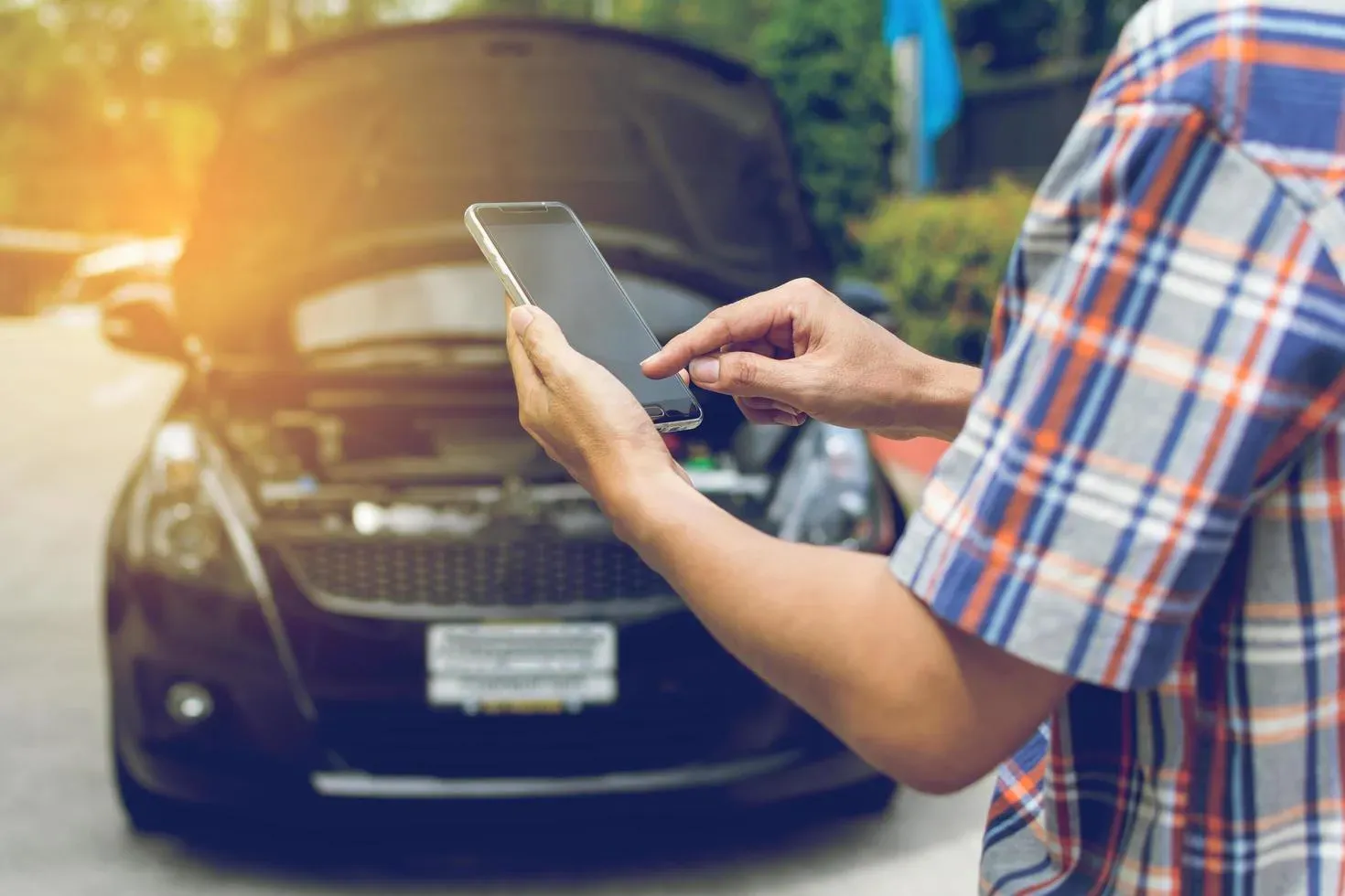 Persona realizando una llamada y de fondo auto con capo levantado