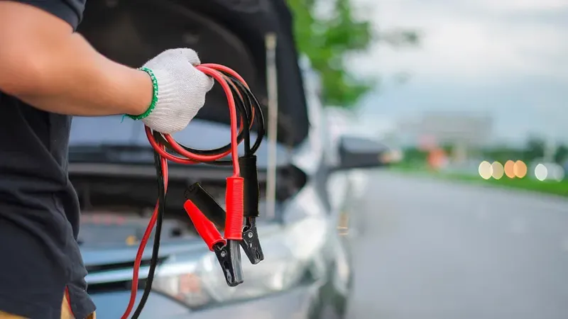 Persona sosteniendo cables de arranque de batería de auto 