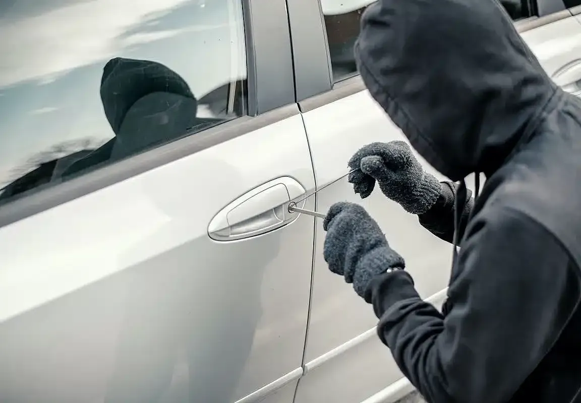 Persona con suéter y capucha forzando cerradura de auto