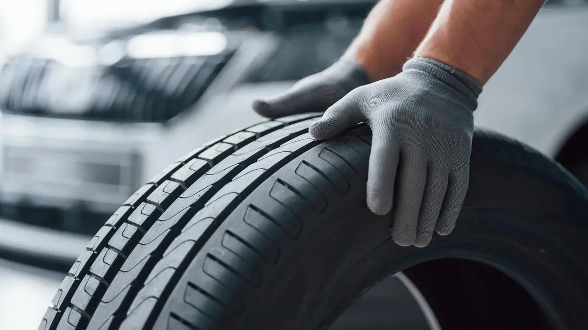 Manos sobre neumático y al fondo auto blanco