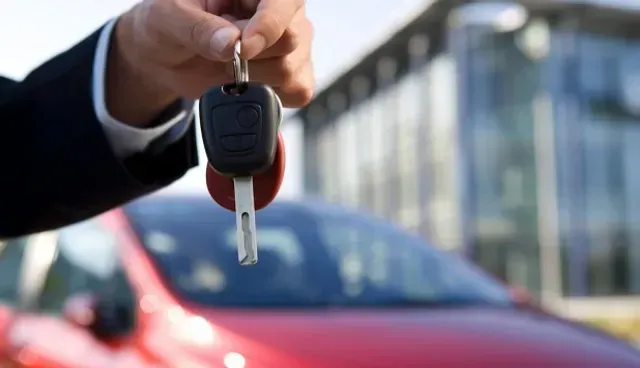 Mano sosteniendo llaves y al fondo un auto rojo