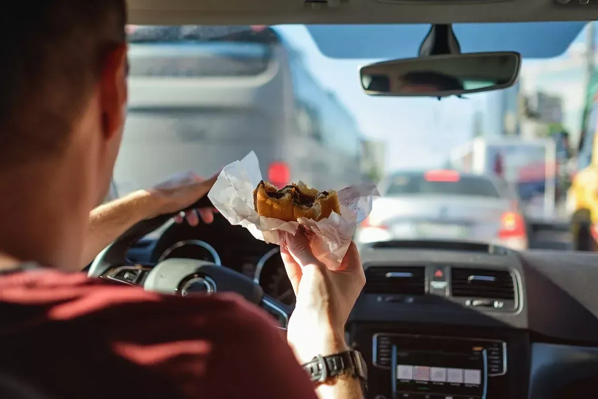 Persona dentro de auto comiendo hamburguesa