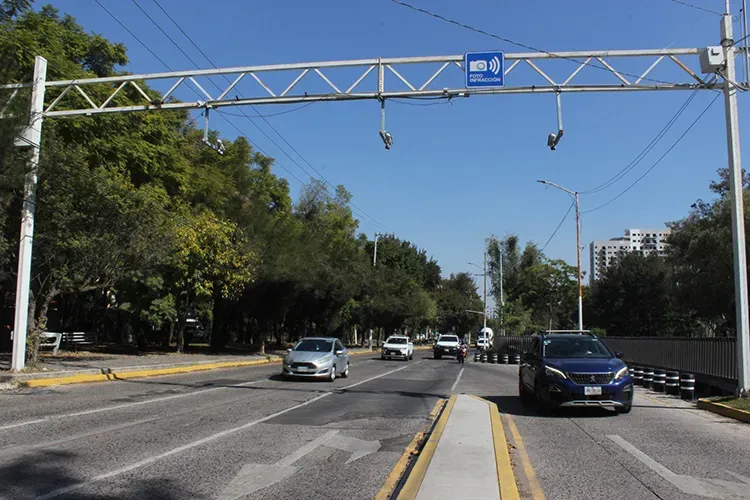 Autos en vía con torre de cámaras de foto multas encima 