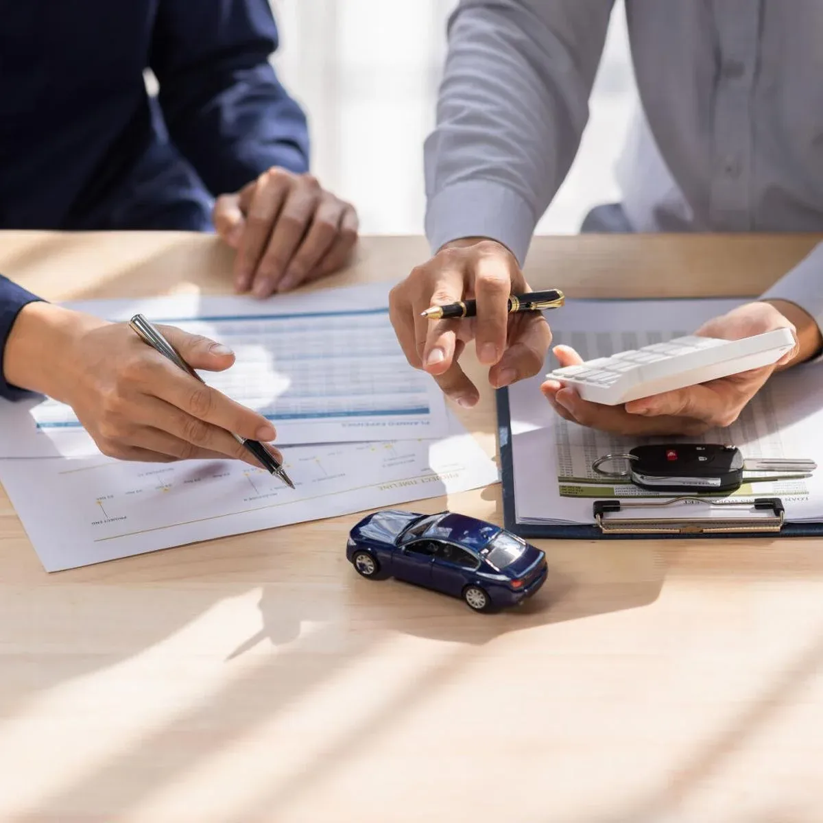 Personas en una mesa con documentos y auto azul a escala