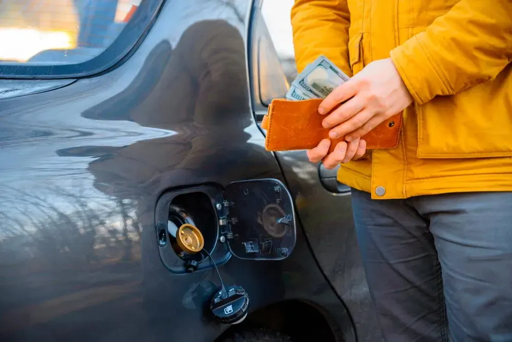 Auto con tapa de combustible abierta y persona al lado con cartera con billetes