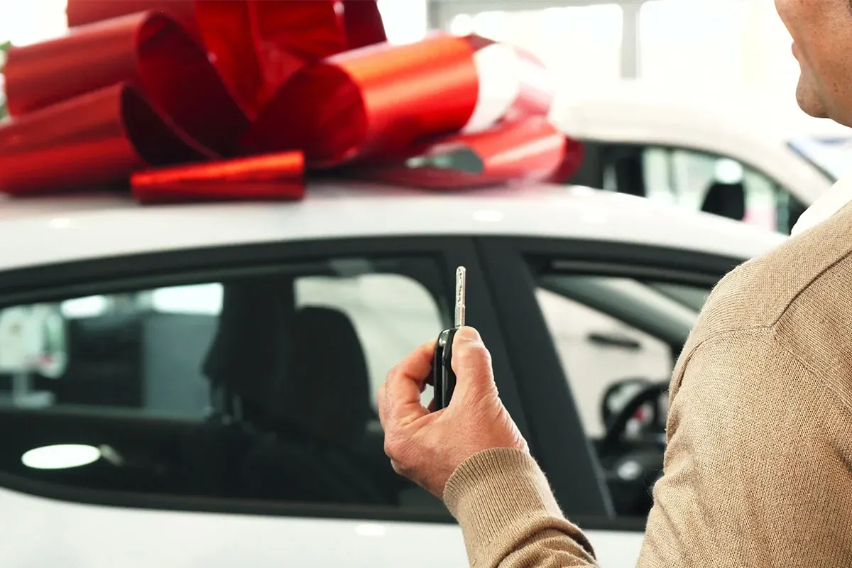 Persona sosteniendo llave de auto frente a un auto con moño rojo