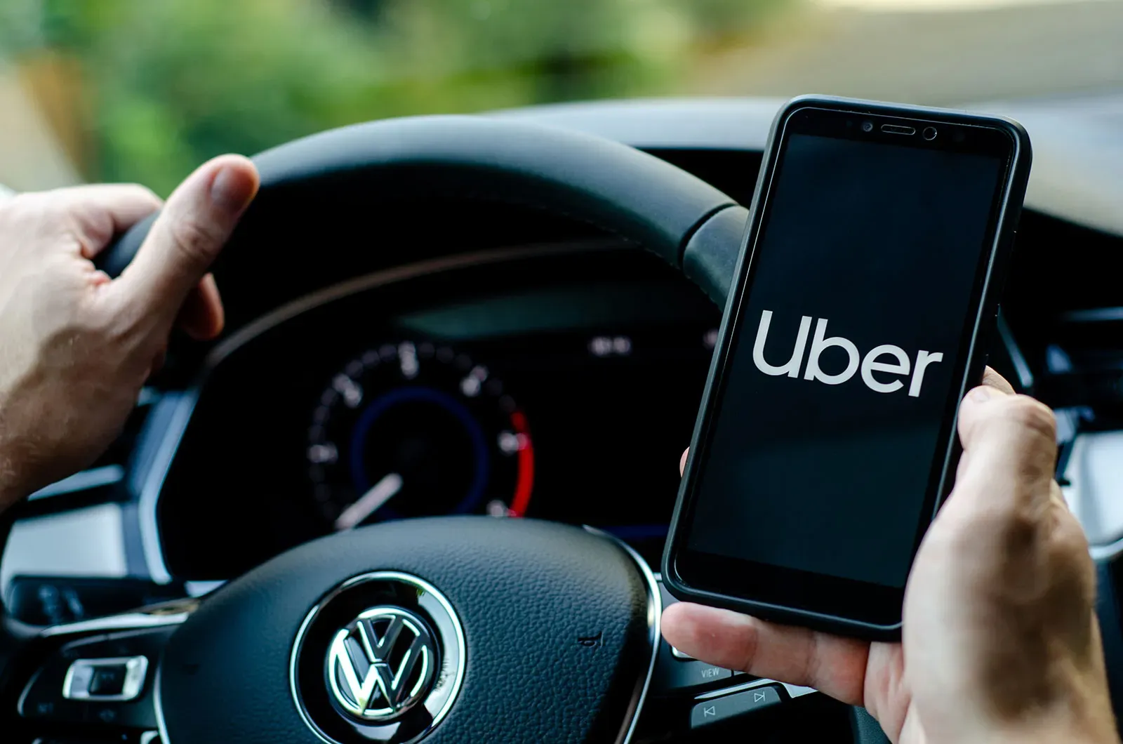 Persona al volante con teléfono en mano con app de Uber 