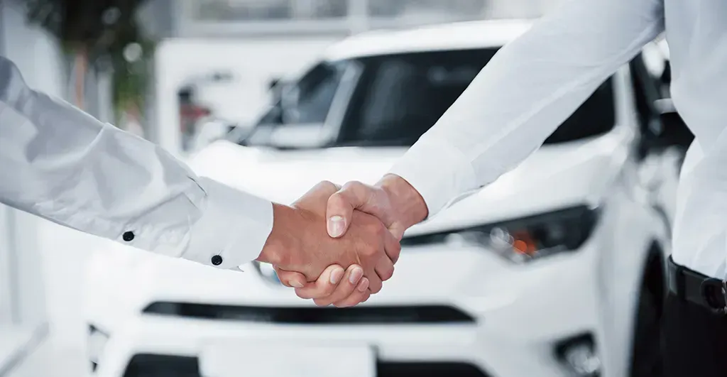 Personas estrechando las manos y al fondo un auto blanco