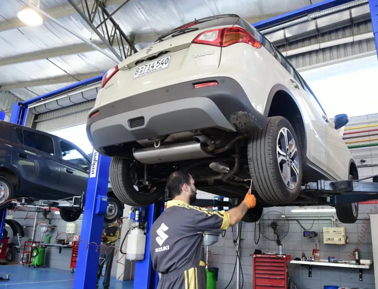 Persona realizando revisión a chasis de camioneta suzuki color blanco sobre una plataforma suspendida en el aire 