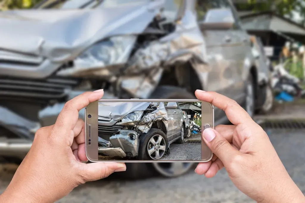 Manos Sosteniendo Teléfono Tomando Foto de un Auto que Sufrió un Accidente 