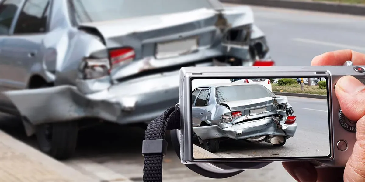 Mano sosteniendo cámara que toma foto de un coche gris chocado en la parte trasera