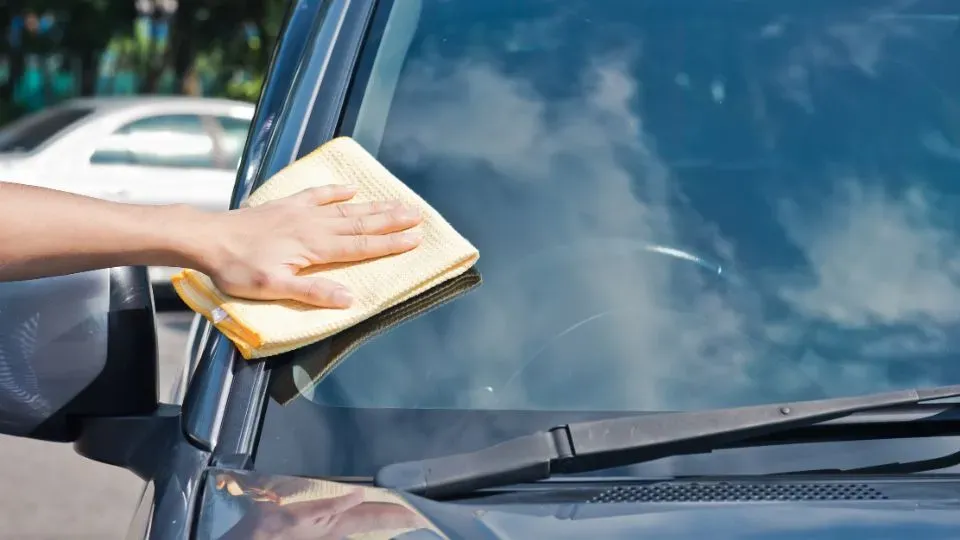 Mano frotando toalla en parabrisas de auto