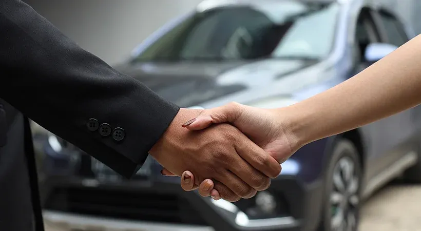 Personas estrechando manos y al fondo un auto gris 