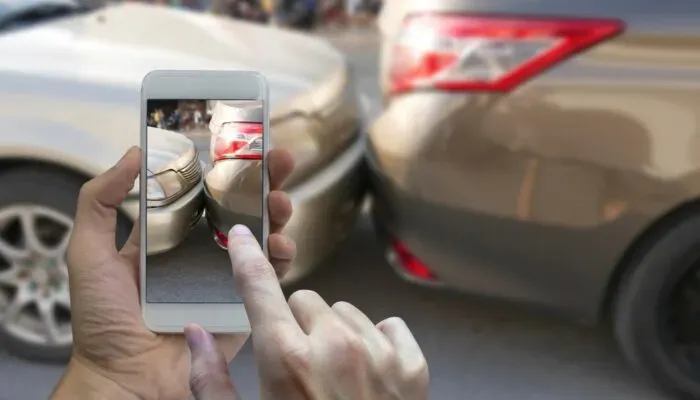 Manos sosteniendo teléfono que toma foto a un choque entre autos 