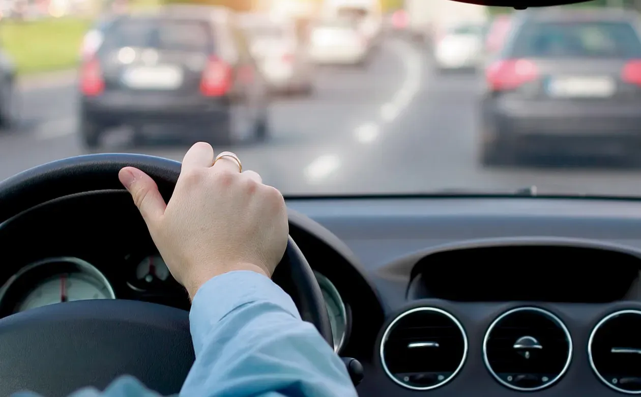 Mano sobre volante de auto que va por carretera transitada por otros autos 