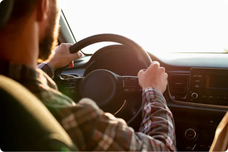 Persona con manos en el volante de auto en un día soleado