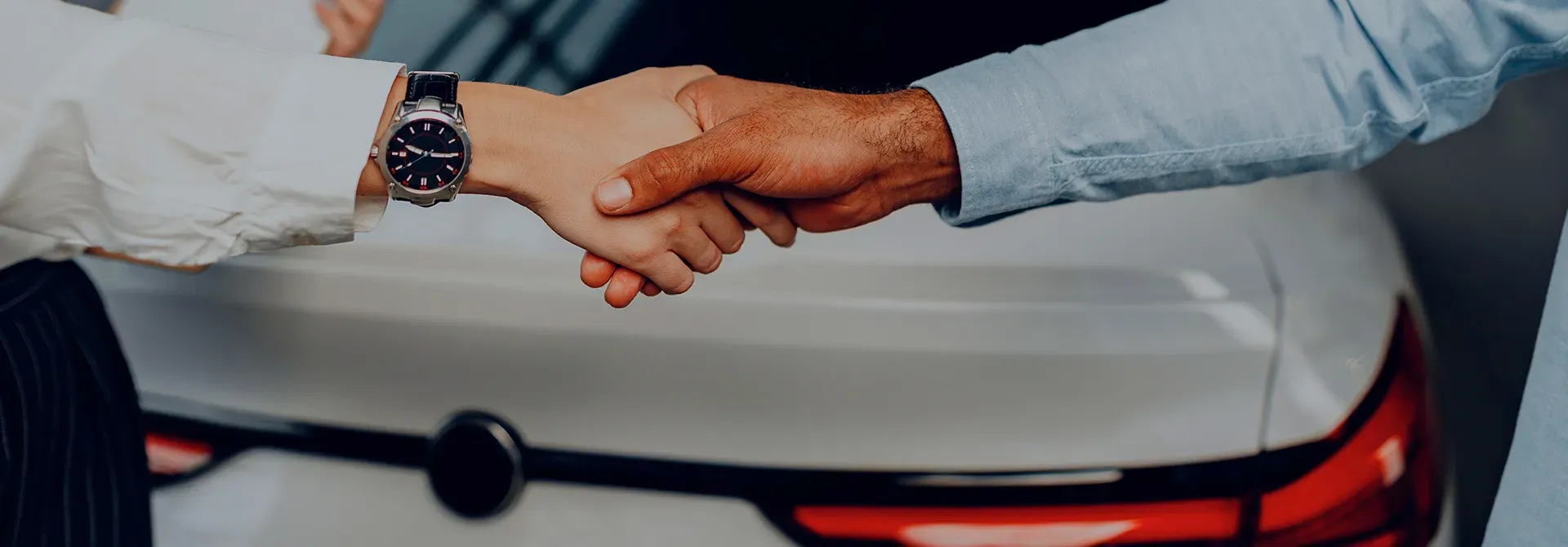 Mano estrechadas y al fondo parte trasera de un auto 