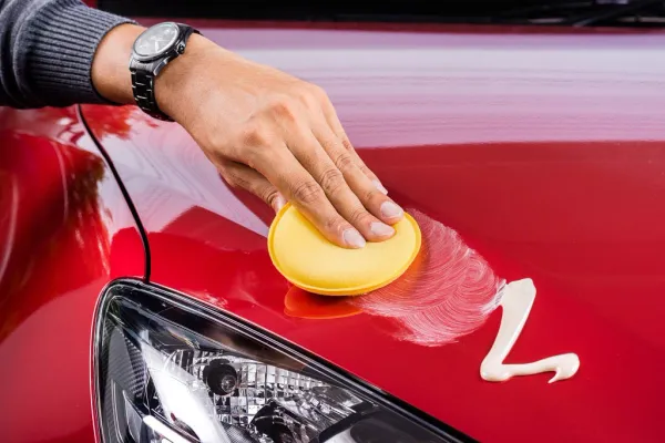 Mano sosteniendo almohadilla de pulido de auto sobre capo de auto rojo