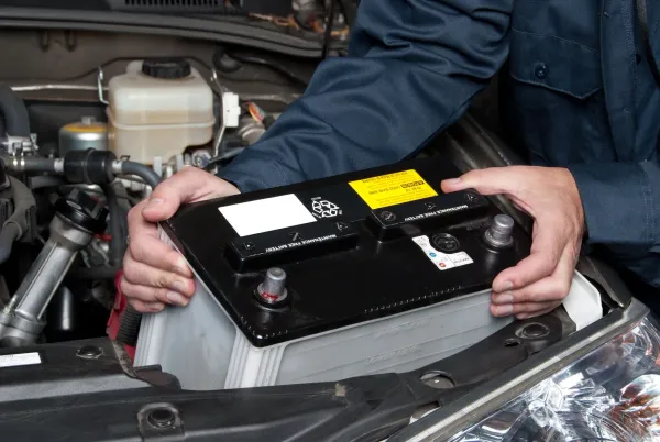 Manos sosteniendo bateria de auto sobre la parte delantera mecánica del auto