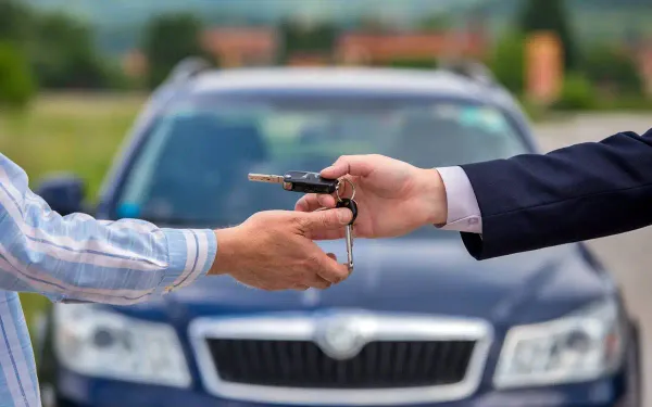 Mano entregando la llaves de auto a otra y un auto azul de fondo