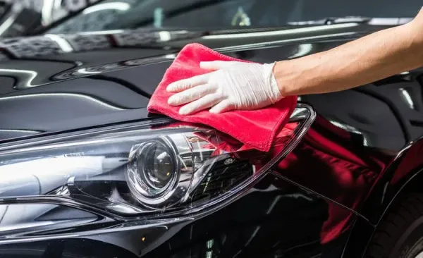 Mano con paño rojo puliendo capo de auto negro