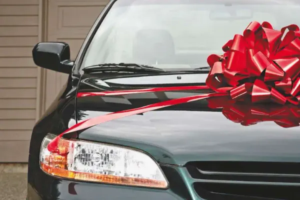 Parte delantera de un auto con un moño rojo en el capo