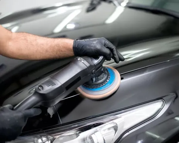 Manos sosnteniendo maquina de pulir autos sobre capo de auto gris