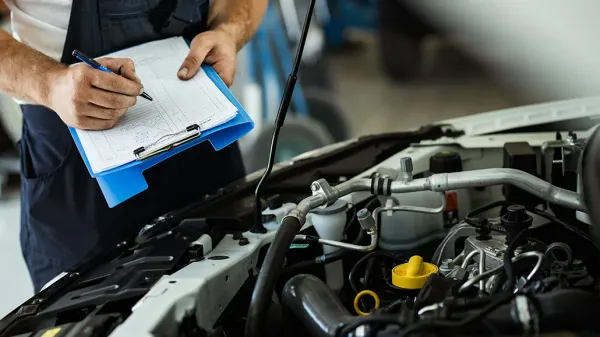 Manos sosteniendo tabla con papel y bolígrafo tomando apuntes de parte mecánica de un auto