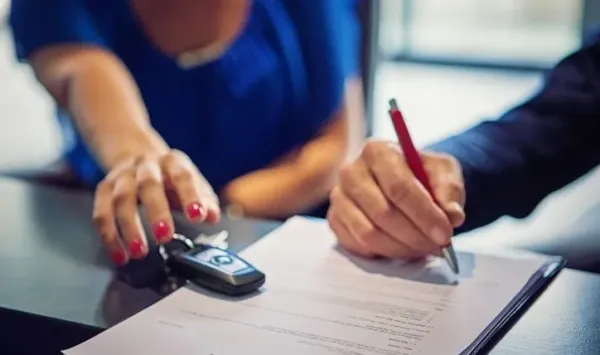 Mano tomando unas llaves de auto y otra firmando con un bolígrafo un contrato