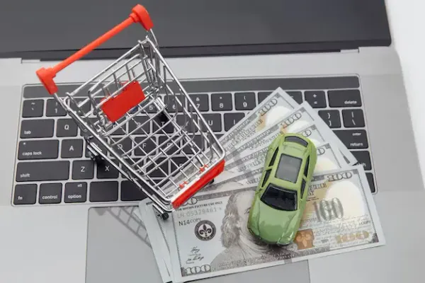 Un carro de compras y auto de collección sobre un par de dolarés y una laptop