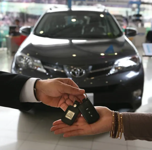 Manos intercambiando llave de auto y de fondo un auto gris