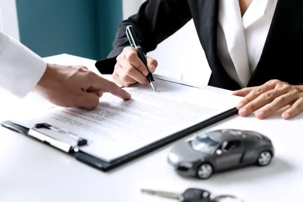 Personas firmando documentos y al lado un auto gris de juguete y unas llaves de auto