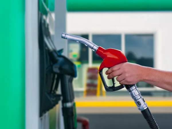 Mano sosteniendo manguera roja de gasolina en estación de servicio